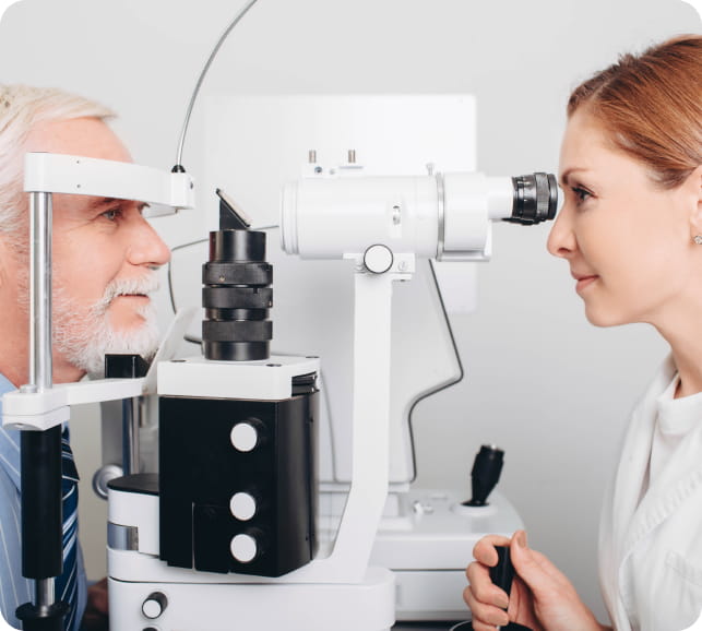 Patient at an eye exam machine (slit‑lamp) while the clinician prepares to examine the retina.